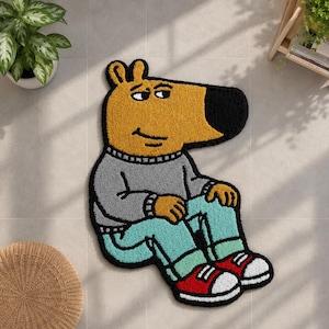May include: A tufted rug shaped like a cartoon character with a yellow head, a large black nose, and a grey sweater. The character wears light blue pants and red sneakers with white soles. The entire figure is outlined in a thick black border.