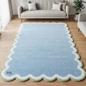 May include: A large, rectangular rug with a scalloped edge. The rug features a gradient of blue hues, transitioning from a darker shade at the bottom to a lighter shade at the top. The border is white and green, with the letters "FFC" in the corner.