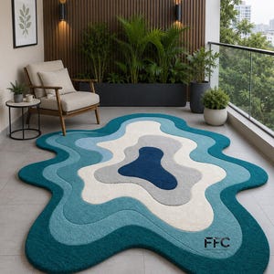 May include: A unique, abstract rug with a layered design in shades of teal, blue, gray, and white. The rug has a wavy, organic shape and is placed on a balcony. The rug's dimensions are not visible in the image.