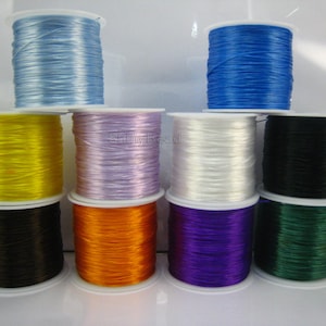 May include: Ten spools of elastic string in various colors, including blue, yellow, purple, white, black, orange, and green. The spools are arranged in three rows on a white surface.
