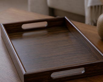 May include: A rectangular dark brown wooden serving tray with a visible wood grain pattern. The tray features a flat base, raised sides, and two integrated cutout handles on opposite ends for carrying. The finish is smooth and polished.