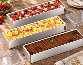 May include: Three rectangular silver metal cake molds filled with desserts. The top mold contains a strawberry and blueberry fruit topping. The middle mold holds diced mango and strawberries. The bottom mold features a cocoa-dusted tiramisu layer.