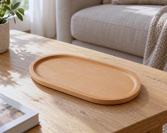 May include: An oval-shaped wooden tray with a smooth, light-toned finish and a raised rim. The tray features a natural wood grain pattern and a shallow, flat base, designed with a simple, clean silhouette and a consistent light brown color throughout.