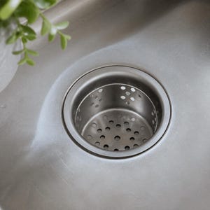 May include: A stainless steel kitchen sink drain strainer with a circular rim and a perforated basket insert. The metal surface has a brushed finish, and the basket features multiple small, evenly spaced circular holes for water drainage.