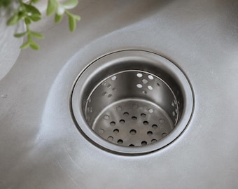 May include: A stainless steel kitchen sink drain strainer with a circular rim and a perforated basket insert. The metal surface has a brushed finish, and the basket features multiple small, evenly spaced circular holes for water drainage.