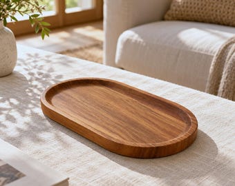 May include: An oval-shaped wooden tray with a smooth, polished surface and visible natural wood grain patterns. The tray features a shallow, recessed center and a raised, rounded rim, showcasing a warm, medium-brown tone throughout.