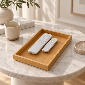May include: A rectangular wooden tray with a light brown finish, containing two white remote controls. The tray features a flat base and raised edges, providing a simple and functional surface for organising small electronic devices.