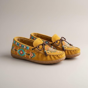 May include: A pair of mustard yellow moccasin-style shoes with intricate Native American-inspired beadwork and embroidery. The shoes feature brown leather laces, tassels, and a stitched sole. The design includes geometric patterns in turquoise, red, and orange.