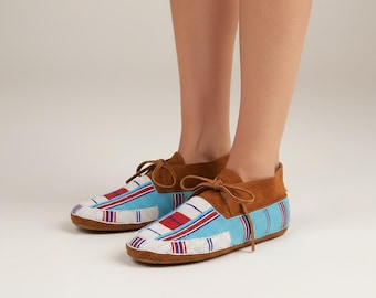 Può includere: Un paio di mocassini con perline con tomaia in pelle scamosciata marrone e un design a righe blu chiaro, bianco e rosso. Le scarpe hanno lacci marroni e una suola marrone. I mocassini sono uno stile di calzatura tradizionale.