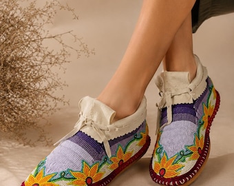 Può includere: Mocassini con perline con colletto e lacci in pelle color crema. Le scarpe presentano un motivo floreale con fiori gialli, arancioni e verdi su sfondo lilla chiaro. Le suole sono rosse.