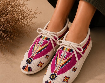Può includere: Un paio di scarpe stringate color bianco sporco con intricate perline in vivaci motivi geometrici magenta, gialli, blu e arancioni. Le scarpe presentano una punta arrotondata, una silhouette bassa e lacci abbinati annodati a fiocco.