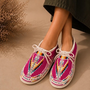 May include: A pair of fuchsia pink low-top sneakers featuring a vibrant, multi-colored geometric beaded pattern on the toe and vamp. The shoes have white laces, white trim along the collar, and a white rubber sole, creating a distinct contrast.