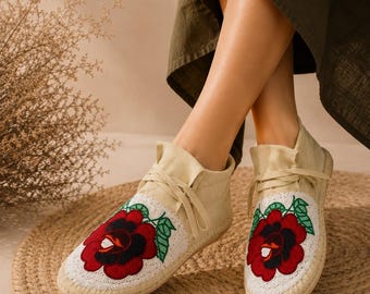Può includere: Scarpe beige in stile espadrillas con un grande motivo floreale rosso e nero con perline sulla punta. Le scarpe hanno una chiusura con lacci e sono posizionate su una suola in juta intrecciata. Le scarpe sono alte circa 15 cm.