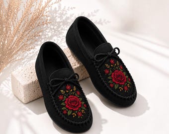 Può includere: Un paio di scarpe slip-on in stile mocassino nero con un fiocco decorativo sulla tomaia e un intricato ricamo di una grande rosa rossa circondata da fiori rossi più piccoli e foglie verdi sulla parte anteriore di ogni scarpa.