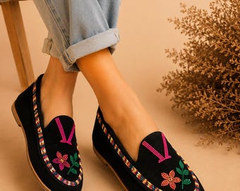 Può includere: Mocassini neri con un bordo di perline multicolori lungo i lati. La parte superiore di ogni scarpa è decorata con una forma a V ricamata in rosa e un motivo floreale composto da un fiore color corallo con foglie verdi su base nera.