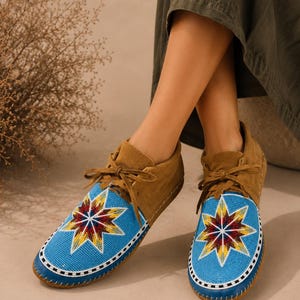 May include: A pair of brown suede moccasins featuring a bright blue beaded vamp with a multi-colored star pattern in red, yellow, and white. The shoes have matching brown suede laces and a white and black beaded border around the toe area.