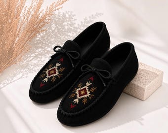 Può includere: Un paio di mocassini neri slip-on con un laccio decorativo sulla tomaia e un intricato ricamo in filo bianco, oro e rosso. Il ricamo presenta un motivo geometrico a forma di stella centrato sulla parte superiore di ogni scarpa.