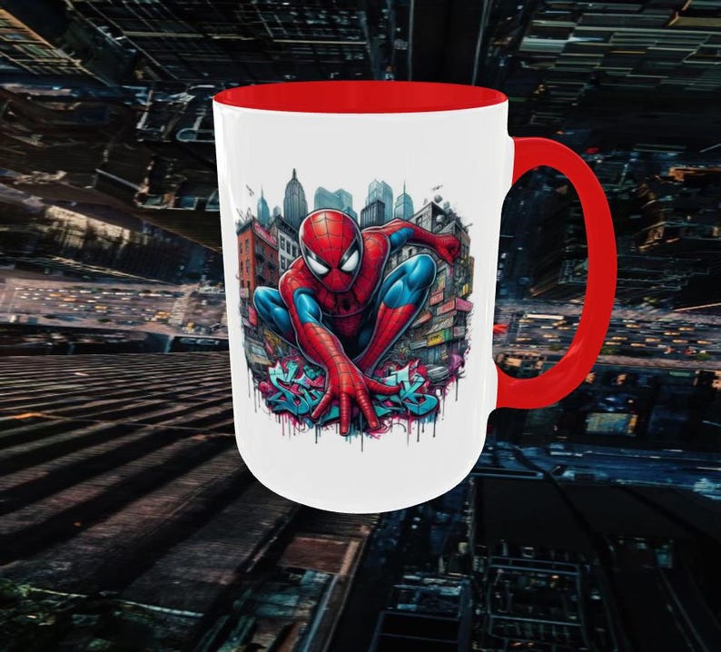 May include: White ceramic mug with a red interior and handle. The mug features a colorful illustration of Spider-Man in a city setting. The design includes graffiti-style lettering at the bottom of the image.