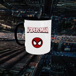 May include: White ceramic mug with a black handle and interior. The mug features the words "SPIDER-MAN" in red and white, along with a red and black spider symbol. The mug is a fan item.