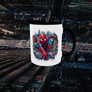 May include: White ceramic mug with a black handle featuring a colorful illustration of Spider-Man in a city setting. The superhero is depicted in his classic red and blue suit, crouching with his hands outstretched.