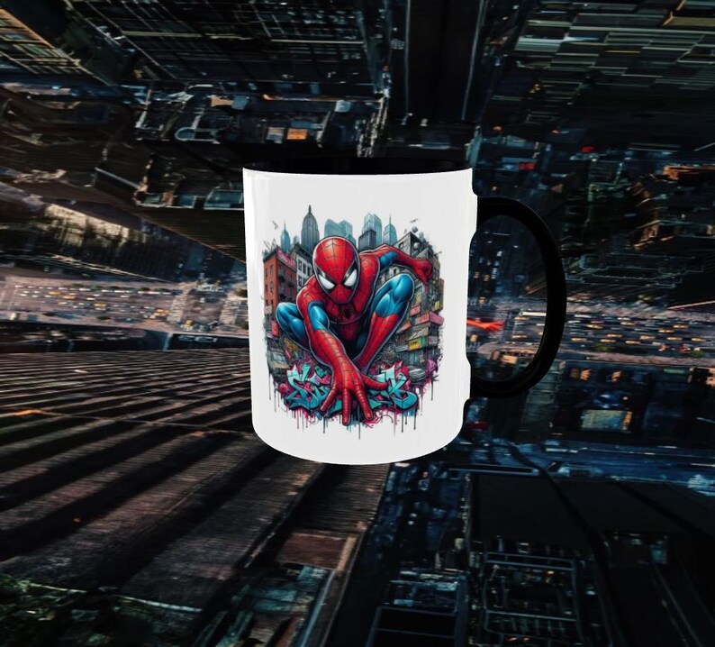 May include: White ceramic mug with a black handle featuring a colorful illustration of Spider-Man in a city setting. The superhero is depicted in his classic red and blue suit, crouching with his hands outstretched.
