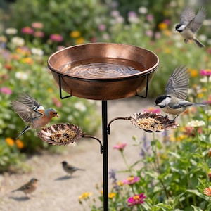 May include: A bronze-colored bird bath with a water basin and two leaf-shaped feeding trays. Several birds are perched on the trays and flying around the bird bath. The bird bath is in a garden with colorful flowers.