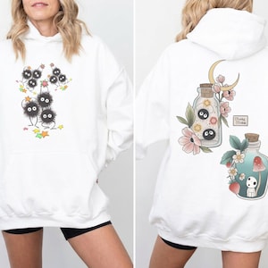 May include: White hoodie with a front graphic of black, fluffy creatures with googly eyes and a back graphic of potion bottles with floral and moon designs. The hoodie has a front pocket and a hood.