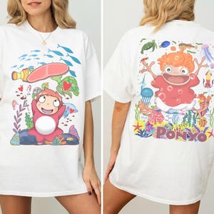 K&ouml;nnte beinhalten: Wei&szlig;es T-Shirt mit einer bunten Cartoon-Grafik einer Figur aus dem Animationsfilm "Ponyo". Das Frontdesign zeigt die Figur mit Meeresbewohnern. Die R&uuml;ckseite des Shirts hat eine gr&ouml;&szlig;ere Illustration der Figur mit dem Wort "PONYO."