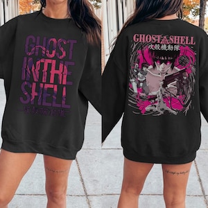 May include: Black sweatshirt featuring the text "GHOST IN THE SHELL" in a gradient purple font on the front. The back displays a pink and white graphic with characters and Japanese text. A crew neck sweatshirt.
