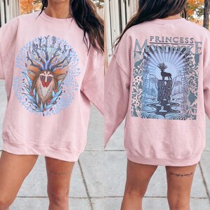 May include: A light pink sweatshirt with a graphic on the front and back. The front features a deer-like creature with a crown of branches and leaves. The back has the text "PRINCESS MONONOKE" above a landscape with a deer silhouette.