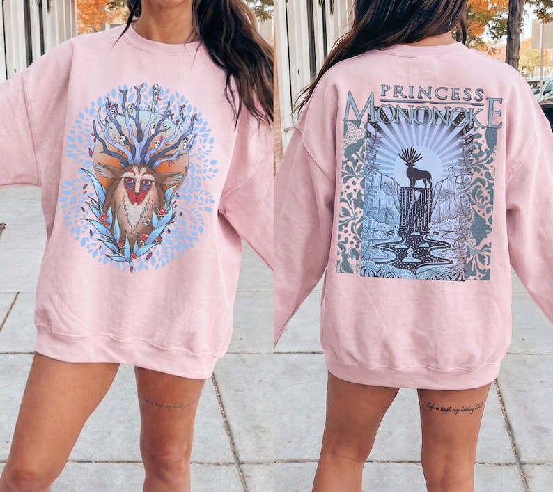 May include: A light pink sweatshirt with a graphic on the front and back. The front features a deer-like creature with a crown of branches and leaves. The back has the text "PRINCESS MONONOKE" above a landscape with a deer silhouette.
