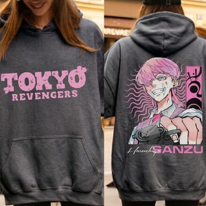 May include: Dark gray hoodie with the text "TOKYO REVENGERS" in pink on the front. The back features a pink-haired anime character with a gun, the name "Haruchiyo SANZU", and pink accents.