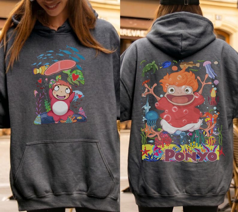 K&ouml;nnte beinhalten: Dunkelgrauer Kapuzenpullover mit einer farbenfrohen Cartoon-Illustration des Films "Ponyo" auf Vorder- und R&uuml;ckseite. Die Vorderseite zeigt die Figur unter einem roten Regenschirm, die R&uuml;ckseite zeigt die Figur mit dem Wort "Ponyo".