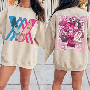 May include: Beige sweatshirt featuring anime characters. The front displays a blue and pink graphic with two characters. The back has a pink framed design with multiple anime figures and Japanese text. A casual, long-sleeved top.