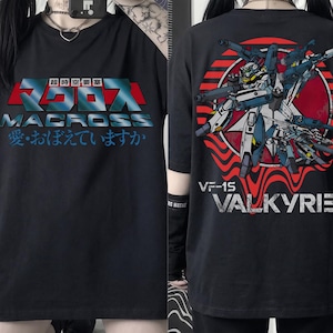 May include: Black t-shirt featuring the word "MACROSS" in red and blue Japanese text on the front. The back of the shirt displays a graphic of a fighter jet with the text "VF-1S VALKYRIE".