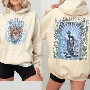 May include: Cream-colored hoodie with a front graphic of a deer-like creature surrounded by blue leaves and a back graphic with the text "PRINCESS MONONOKE" above a deer silhouette and waterfall scene. The hoodie has a front pocket and a hood.