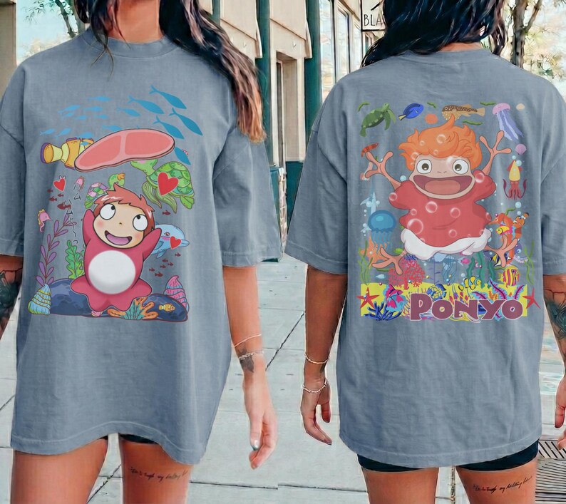 K&ouml;nnte beinhalten: Ein blau-graues T-Shirt mit einem Cartoon-Motiv der Figur "Ponyo" aus dem Animationsfilm. Das Frontdesign zeigt die Figur mit Meeresbewohnern. Das R&uuml;ckendesign zeigt die Figur mit dem Wort "Ponyo".