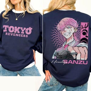 May include: Navy blue sweatshirt with the text "TOKYO REVENGERS" in pink on the front. The back features an anime illustration of a character with pink hair and the name "Haruchiyo SANZU".