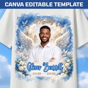May include: A white t-shirt featuring a memorial graphic with a portrait of a smiling person, large white angel wings, blue clouds, white flowers, and the text "IN LOVING MEMORY", "Oliver Bennett", and the dates "12-04-2026" and "05-05-1998".
