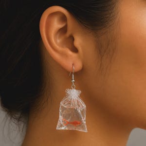 Peut inclure: Boucles d'oreilles fantaisie avec un design de sac en plastique transparent, chacune contenant un petit poisson orange. Les boucles d'oreilles sont suspendues à des crochets argentés. Un accessoire unique et amusant.