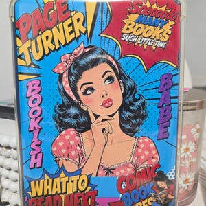 May include: A rectangular tablet case featuring a pop art illustration of a person with dark hair and a pink headband. The design includes text reading PAGE TURNER, SOOOOOOO MANY BOOKS SUCH LITTLE TIME, BOOKISH BABE, WHAT TO READ NEXT, and COMIC BOOK VIBES.