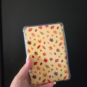 May include: A rectangular tablet case featuring a light yellow background patterned with a variety of colourful autumn leaves in shades of red, orange, brown, and purple. The case has a clear, transparent protective border with reinforced corners.