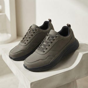 Può includere: Un paio di scarpe da ginnastica verde oliva con finitura opaca liscia, lacci in tinta e una spessa suola nera scanalata. La fodera interna è nera e il design include una linguetta sul tallone per una silhouette bassa e funzionale.