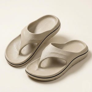 May include: A pair of beige thong sandals featuring a molded footbed with a subtle swirling texture and a thick sole accented by a thin black horizontal stripe running along the side of the platform. The sandals have a wide, smooth strap design.