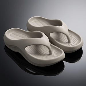 May include: A pair of light beige flip-flops. The sandals have a contoured footbed and a thong-style strap. The soles have a textured design for grip. The flip-flops are made of a soft, flexible material.