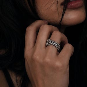 Op de afbeelding: Een zilveren ring met een gedetailleerd, getextureerd tak- of twijgontwerp dat om de vinger wikkelt. Het metaal heeft een gepolijste afwerking met donkere verdiepte delen om het ingewikkelde, organische patroon van de kleine takjes te benadrukken.