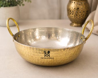 Puede incluir: Un cuenco de servicio redondo de metal martillado con exterior dorado e interior plateado. Cuenta con dos asas de anillo doradas fijadas con remaches en los lados opuestos. El texto METALMINGLE está impreso en negro en la parte frontal.