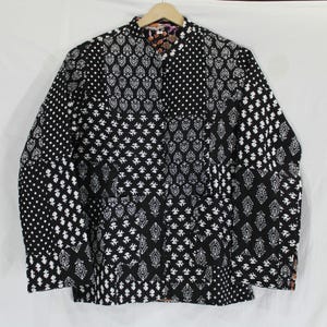 May include: Black and white patterned jacket with a mandarin collar. The jacket features a patchwork design with various geometric and floral patterns. It is hanging on a wooden hanger against a white background.