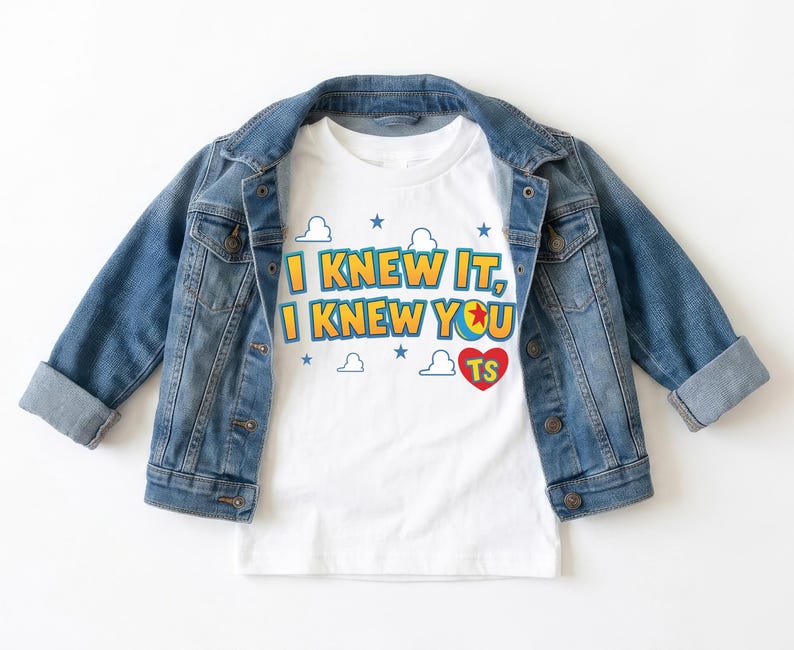K&ouml;nnte beinhalten: Ein wei&szlig;es kurz&auml;rmeliges T-Shirt mit dem Text I KNEW IT, I KNEW YOU, einer bunten Ballgrafik und einem roten Herz mit den Buchstaben TS, umgeben von blauen Sternen und wei&szlig;en Wolkenumrissen, getragen unter einer blauen Jeansjacke.