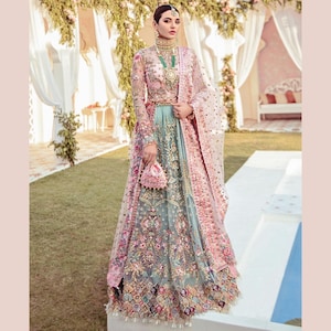 May include: A long-sleeved pale pink bodice with intricate floral embroidery and a high neckline, paired with a voluminous, floor-length light blue skirt featuring heavy multi-colored floral embellishments and a matching sheer pink dupatta.
